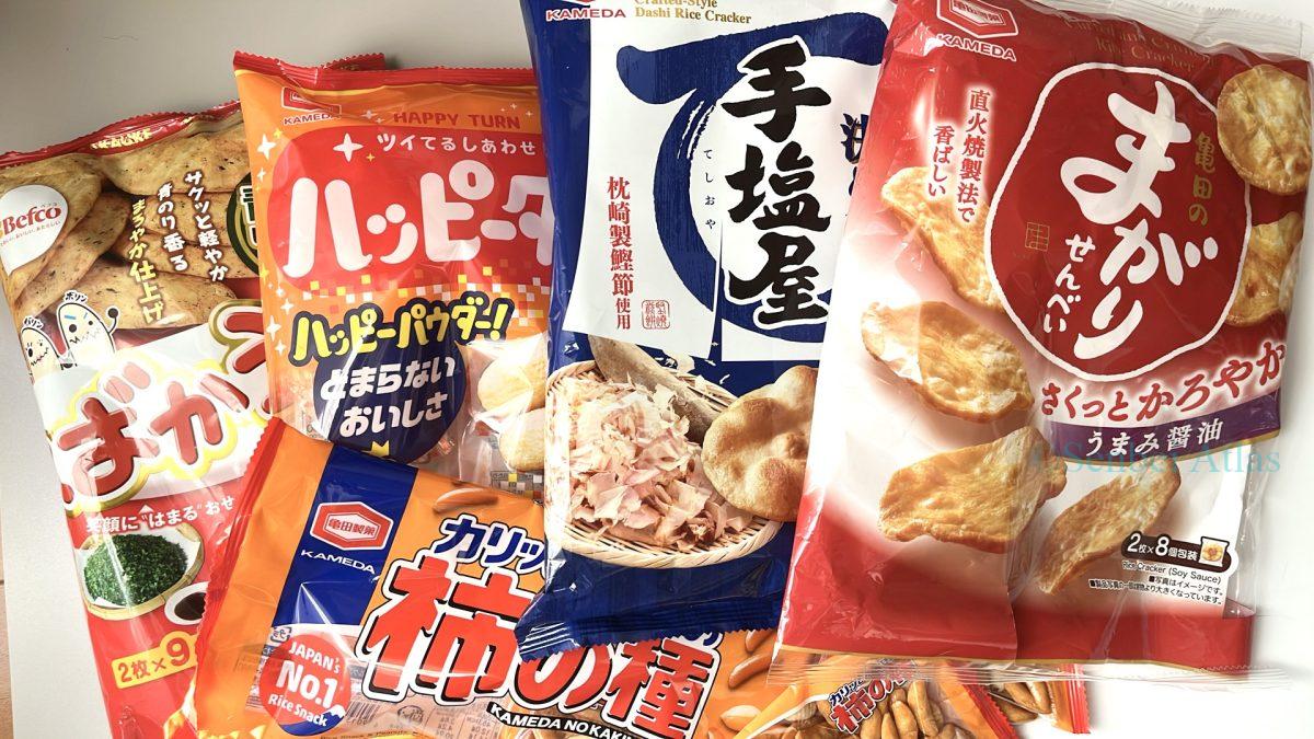 Various types of Japanese rice crackers (Senbei) in their packages: Bakauke (ばかうけ), Teshioya (手塩屋), Magari Senbei (まがりせんべい), Happy Turn (ハッピーターン), and Kaki-no-Tane (柿の種).