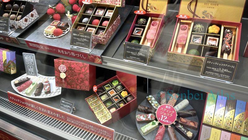 A colorful show window display of BEL AMER (ベルアメール) chocolates at the Amour du Chocolat (アムール・デュ・ショコラ) event (バレンタイン催事) in Shinjuku Takashimaya (新宿高島屋). The display features a variety of beautifully decorated sweets, showcasing the festive atmosphere.