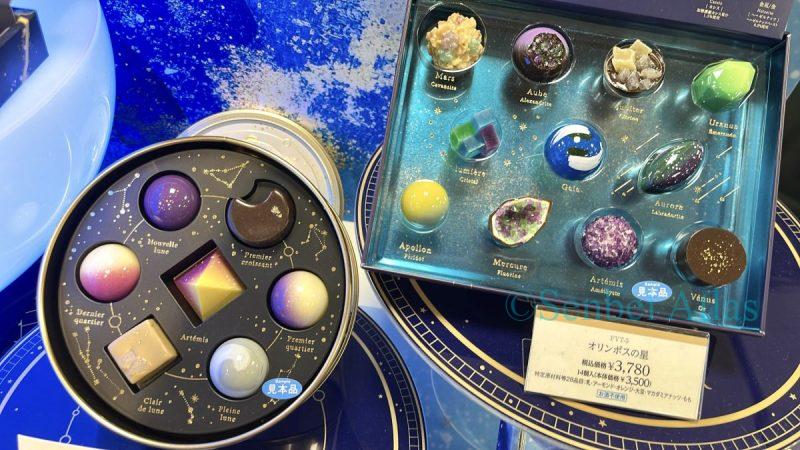 Detailed shot of Foucher Olympus (フーシェ オリンポス) chocolates, featuring glossy, spherical purple and blue chocolates inspired by planets. The set includes unique planet-shaped chocolates representing Mercury, Venus, Earth, and Mars