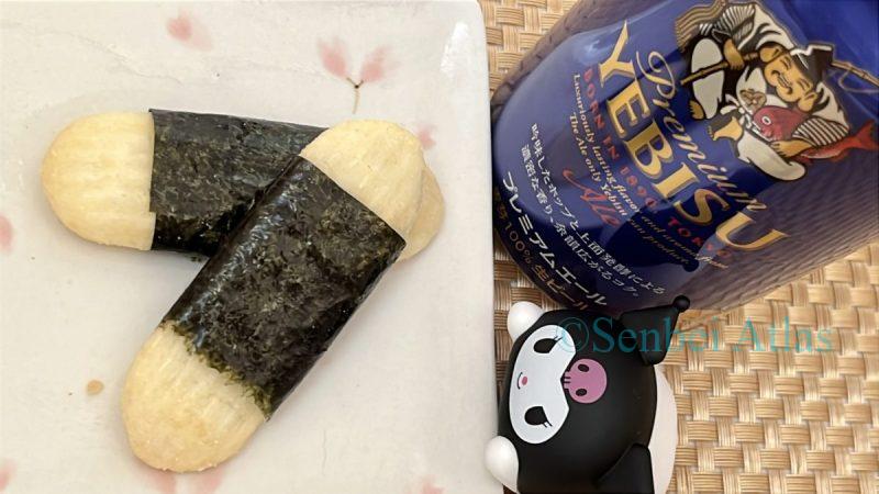 A Happy Turn senbei (Japanese rice cracker) with a DIY nori wrap on a plate, while a Kuromi figure peeks over the edge. A glass of beer is visible in the background.