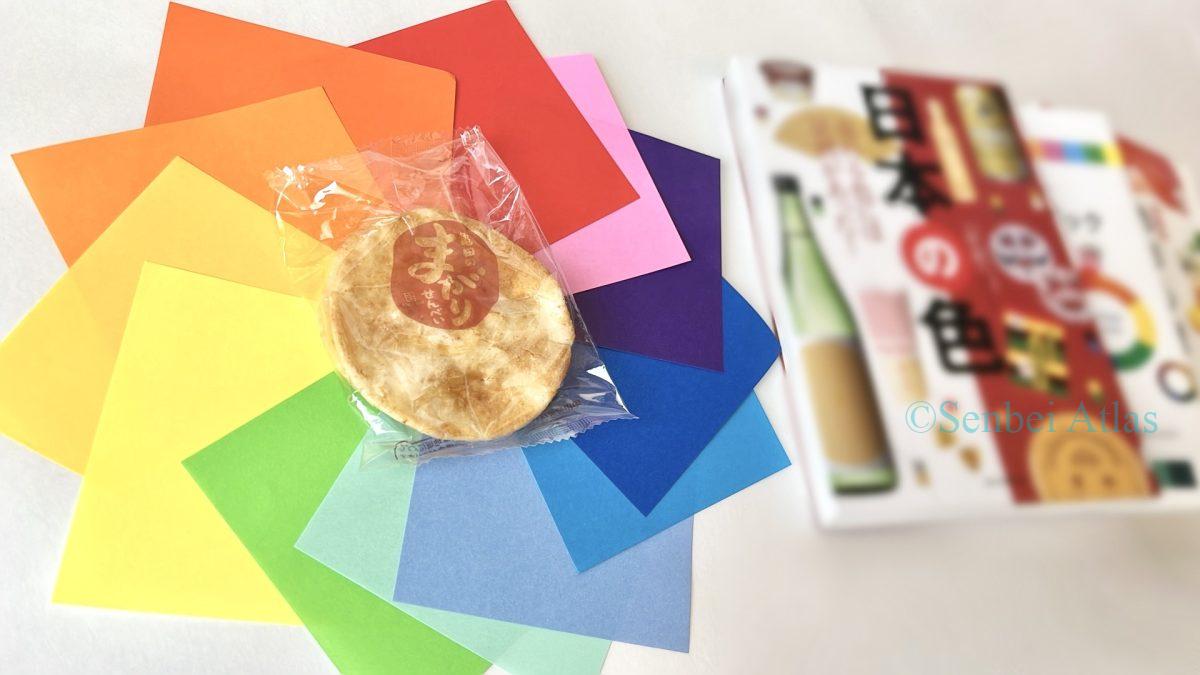 A conceptual photo of senbei package color strategy, featuring colorful origami arranged like a color wheel around a rice cracker and color theory books.