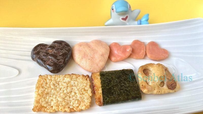 A plate with Akasaka Kakiyama "Heart Mix"  (柿山のハートミックス) contents, including heart-shaped crackers and Arare, with a Palafin (Irukaman) figure in the background.