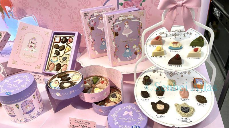 Twotea Room's display at the Amour du Chocolat (アムール・デュ・ショコラ) event at Shinjuku Takashimaya (新宿高島屋). The pale pink booth features chocolates in book-shaped packages and chocolates shaped like cakes and teapots displayed on a two-tier afternoon tea stand.
