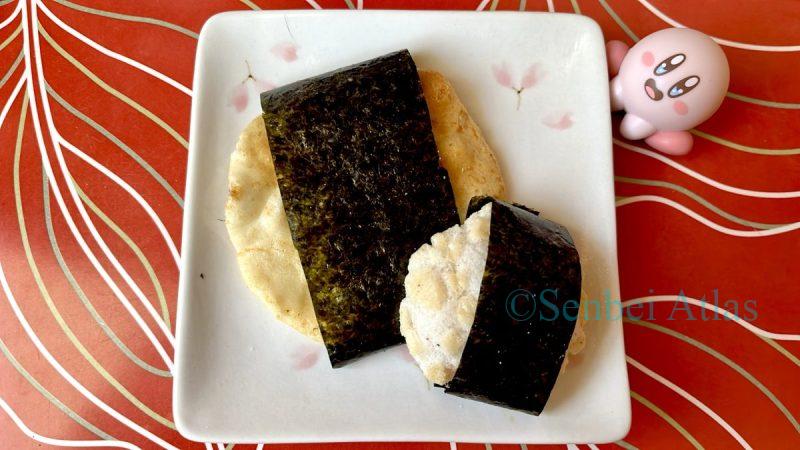 A Kirby figure intensely staring at Magari Senbei & Seto Shio (Japanese rice cracker) wrapped in nori seaweed on a plate. Part of a licensed cook's flavor review series.