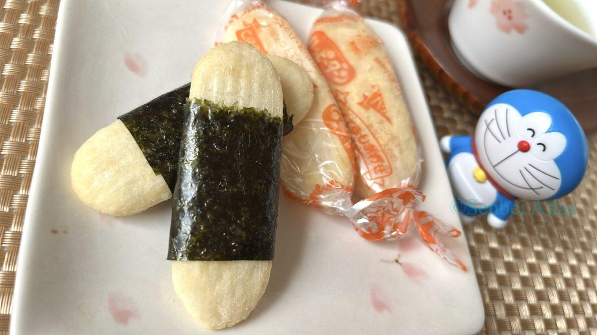 Individually wrapped Happy Turn (ハッピーターン) and a seaweed-wrapped Happy Turn on a plate. A Doraemon (ドラえもん) figure and a Japanese teacup are visible in the background.