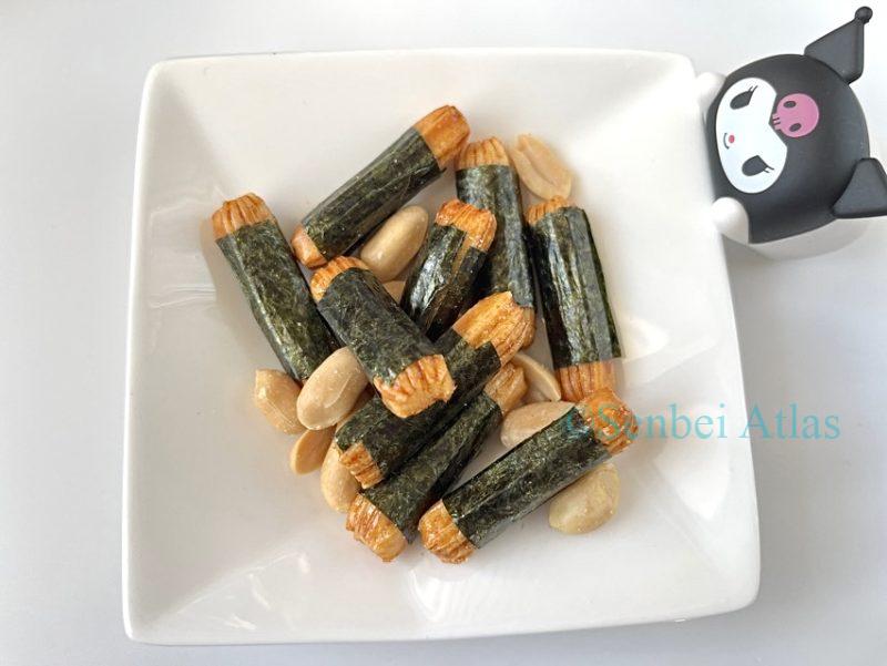 A close-up of Nori-p Pack (海苔ピーパック) contents: seaweed-wrapped rice crackers (Norimaki / 海苔巻き) and peanuts with a Kuromi (クロミ) figure at the corner of the plate.