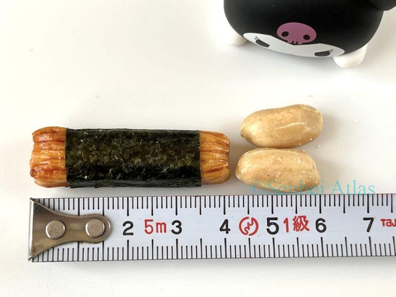 Size measurement of a seaweed-wrapped rice cracker (Norimaki / 海苔巻き) and a peanut from the Nori-p Pack (海苔ピーパック) using a measuring tape, with a Kuromi (クロミ) figure in the background.