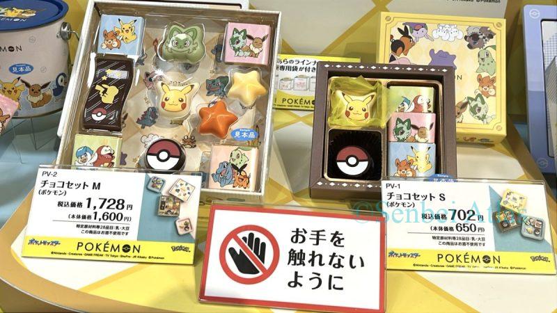 Two boxes of Pokémon chocolates (ポケモンチョコ) displayed side-by-side, featuring chocolates shaped like Pikachu (ピカチュウ), Sprigatito (ニャオハ), and Poké Balls. A sign is placed asking visitors not to touch the exhibit, as the display is popular with families.