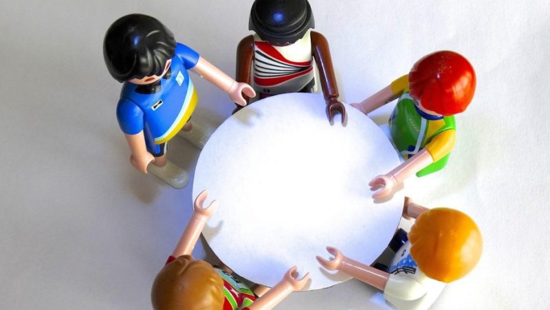 Five LEGO (レゴ) minifigures gathered around a round table for a meeting or social gathering.