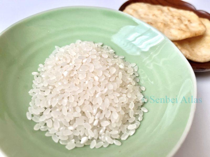Raw rice (生米) in the foreground with Japanese rice crackers (Senbei / せんべい) in the background.