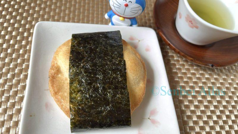 Teshioya (Japanese rice cracker) with dashi flavor being tested with a DIY seaweed wrap. Background features a Doraemon figure and a traditional teacup.