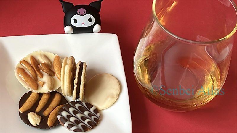 A plate of DIY chocolate senbei made with Kaki-no-Tane (柿の種) and Peti Usuyaki (プチ薄焼き) next to a glass of brandy with a Kuromi (クロミ) Figure for Valentine's Day.