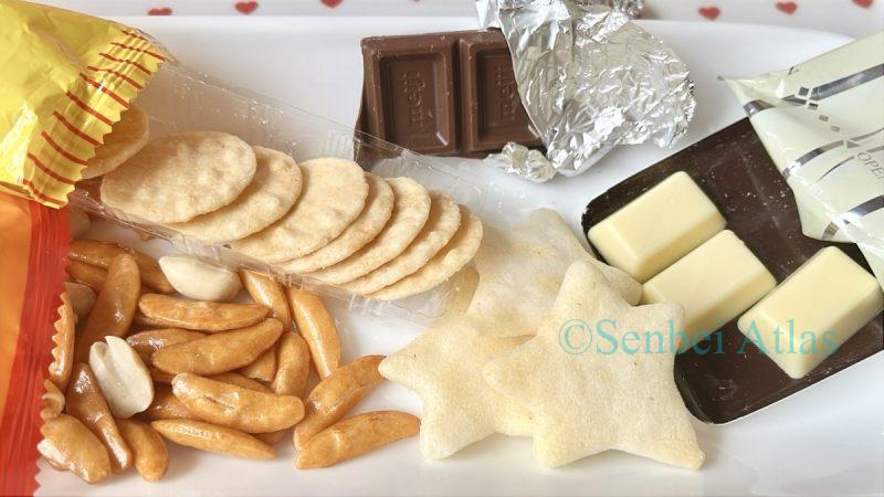 Three types of senbei (Kaki-no-Tane (柿の種), Petit Usuyaki (プチうす焼), Chiisana Hoshi Tabeyo (小さな星たべよ)) and two types of chocolate on a plate.