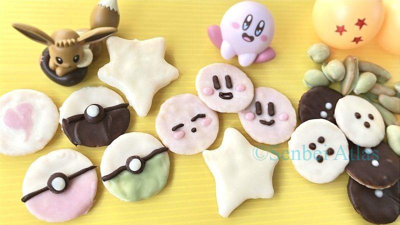 An assortment of chocolate senbei (せんべい) inspired by Poké Balls (ポケボール), Kirby (カービィ), Dragon Ball (ドラゴンボール), and Senzu Beans (仙豆) on a single plate, with Eevee (イーブイ), Kirby, and Dragon Ball items in the background.