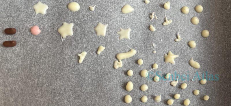 Various chocolate dots and stars drawn on parchment paper for piping practice while making anime-themed snacks.