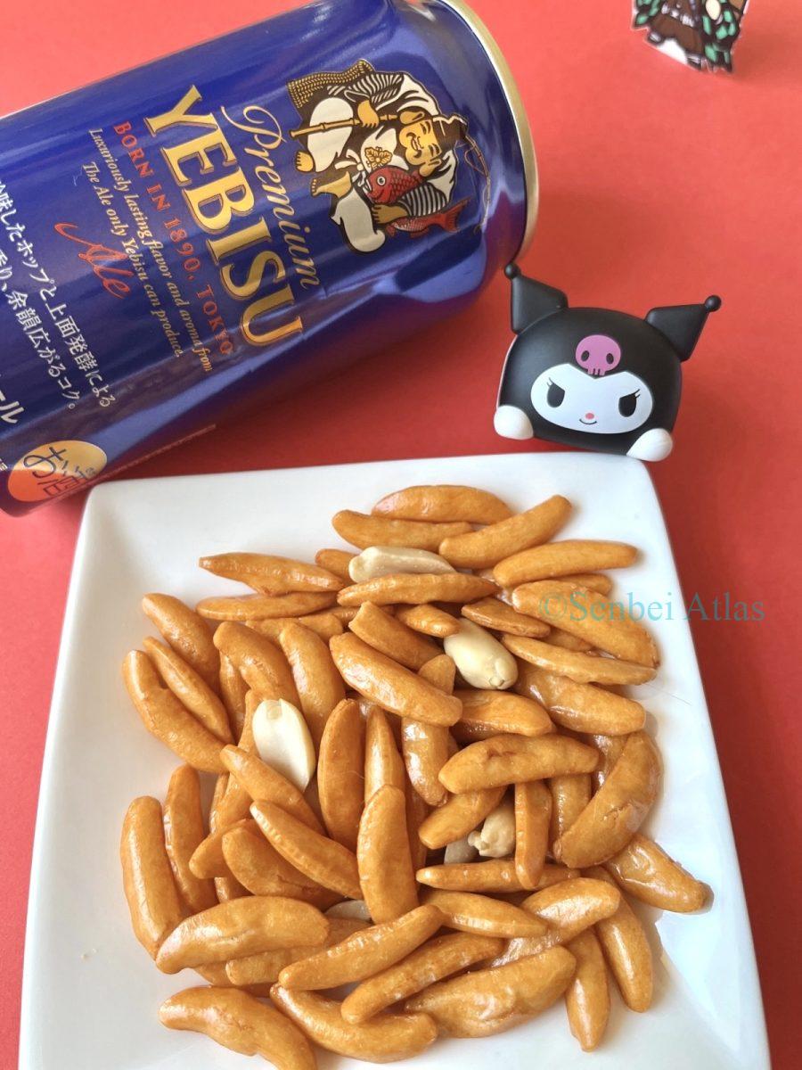 A plate of Kaki-no-Tane (柿の種) with a can of Yebisu Beer (ヱビスビール) and a Kuromi (クロミ) figure touching the plate.