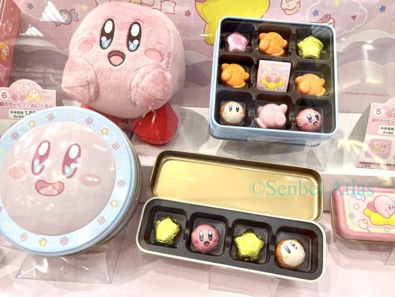 The can contains chocolates in the shape of Kirby (カービィ). The can lid has a smiling Kirby on it, and the Kirby plush toy next to it is also smiling.