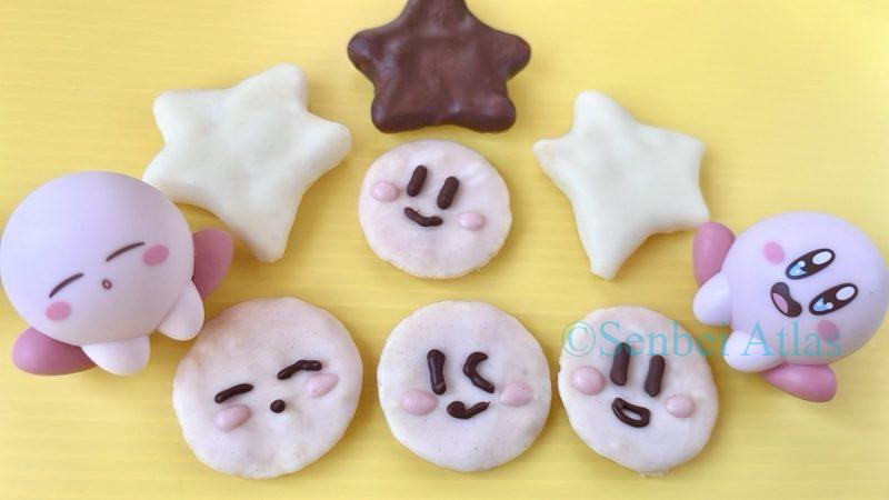 Four pink chocolate senbei (せんべい) featuring Kirby (カービィ) faces and three star-shaped ones, with expressions matching the Kirby figure standing next to them.
