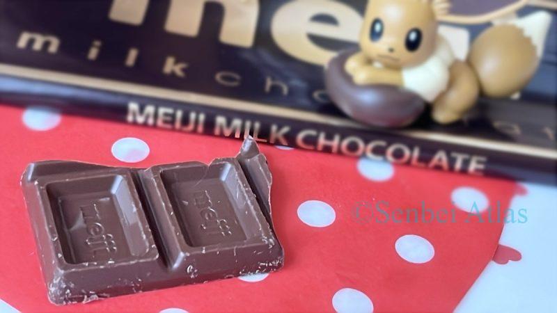 A partial view of a Meiji Milk Chocolate (明治ミルクチョコレート) bar in the foreground with an Eevee (イーブイ) figure in the background.