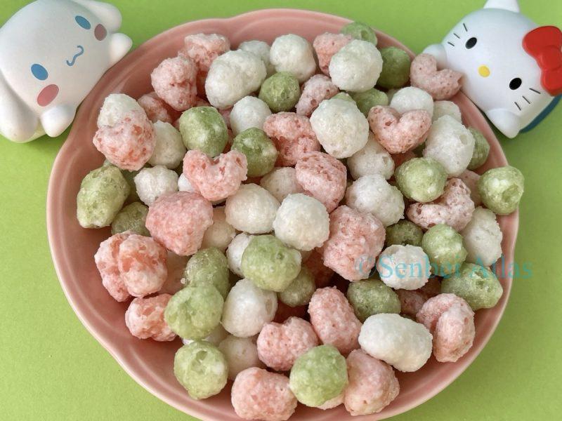 Colorful Hina-arare (ひなあられ) with Hello Kitty (ハローキティ) and Cinnamoroll (シナモロール) figures in the background.