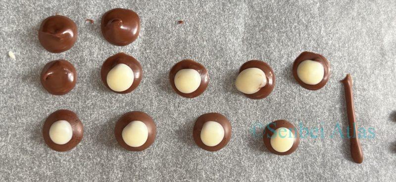 Small round chocolates with a white center and milk chocolate border on parchment paper, prepared for the center of the Poké Ball (ポケボール) design.