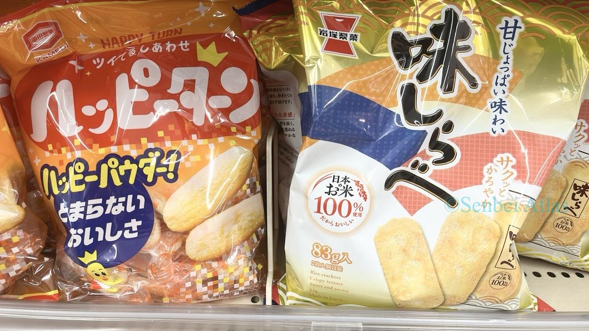 A supermarket shelf in Japan showing Happy Turn (ハッピーターン) and Ajishirabe (味しらべ) displayed side-by-side.