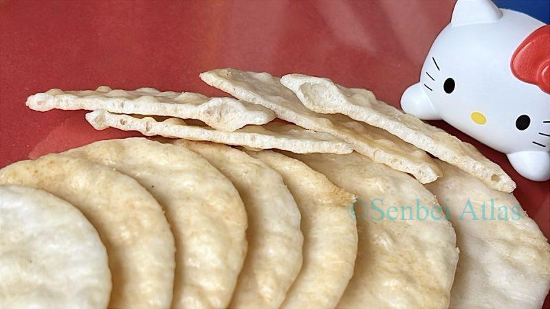 A row of thin senbei (薄焼きせんべい) , showing a cross-section with Hello Kitty (ハローキティ) in the background.